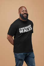 Load image into Gallery viewer, Smiling African man wearing black short sleeve tee with Crenshaw Walks across the front. Design is done in a stencil style and slightly slanted up.