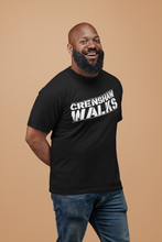 Load image into Gallery viewer, Smiling African man wearing black short sleeve tee with Crenshaw Walks across the front. Design is done in a stencil style and slightly slanted up.
