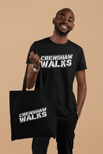 Load image into Gallery viewer, African man wearing black short sleeve tee with Crenshaw Walks across the front. The man is holding a matching black tote bag. The Crenshaw Walks design is done in a stencil style and slightly slanted up.
